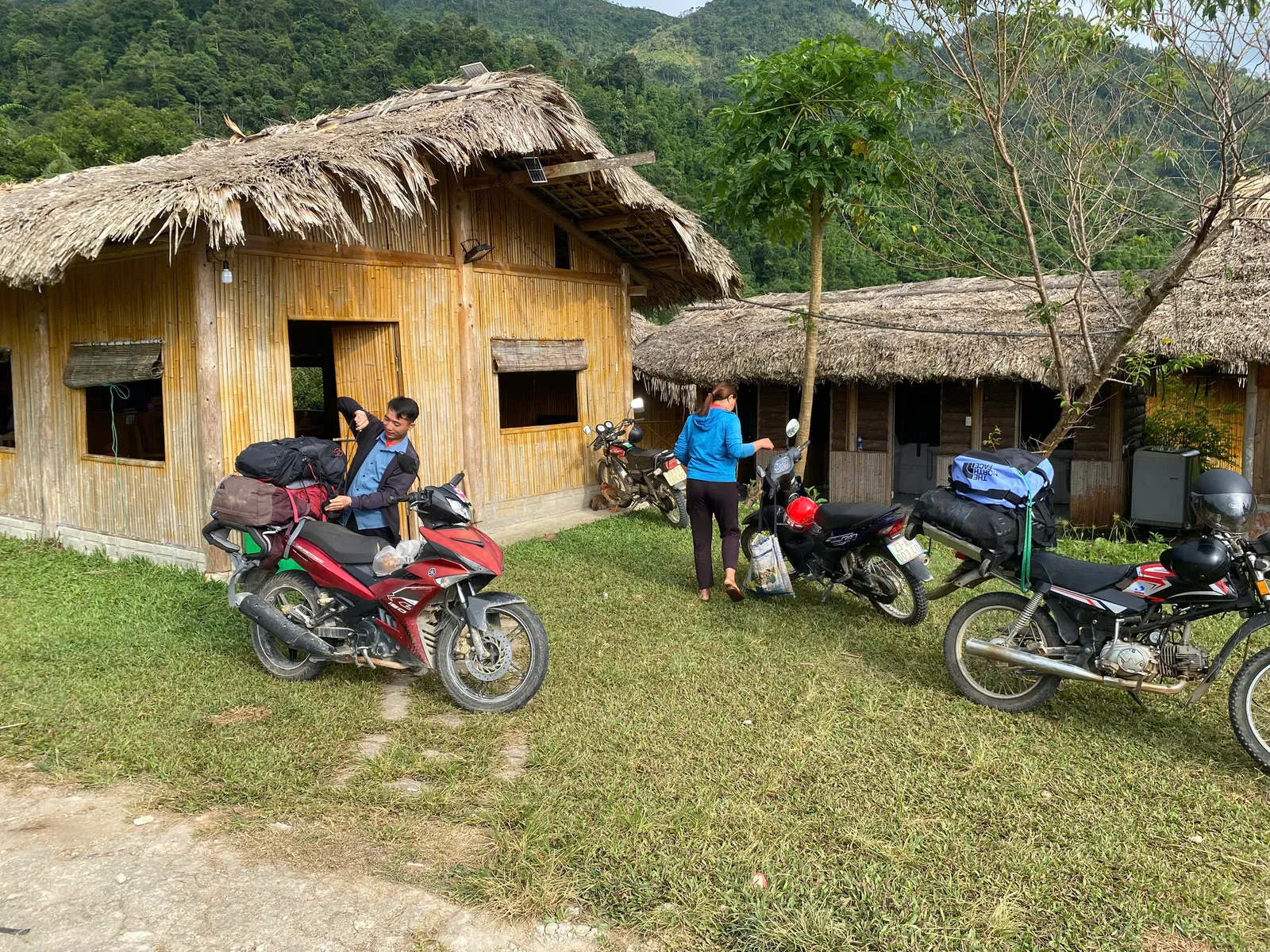 Trekkers hand luggage to a driver beside a motorbike at a village trailhead during the Ban Luoc traverse, Hoang Su Phi.