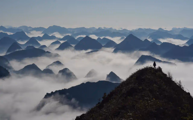 Lone trekker on a ridge above an endless sea of clouds and karst peaks at Chieu Lau Thi sunrise