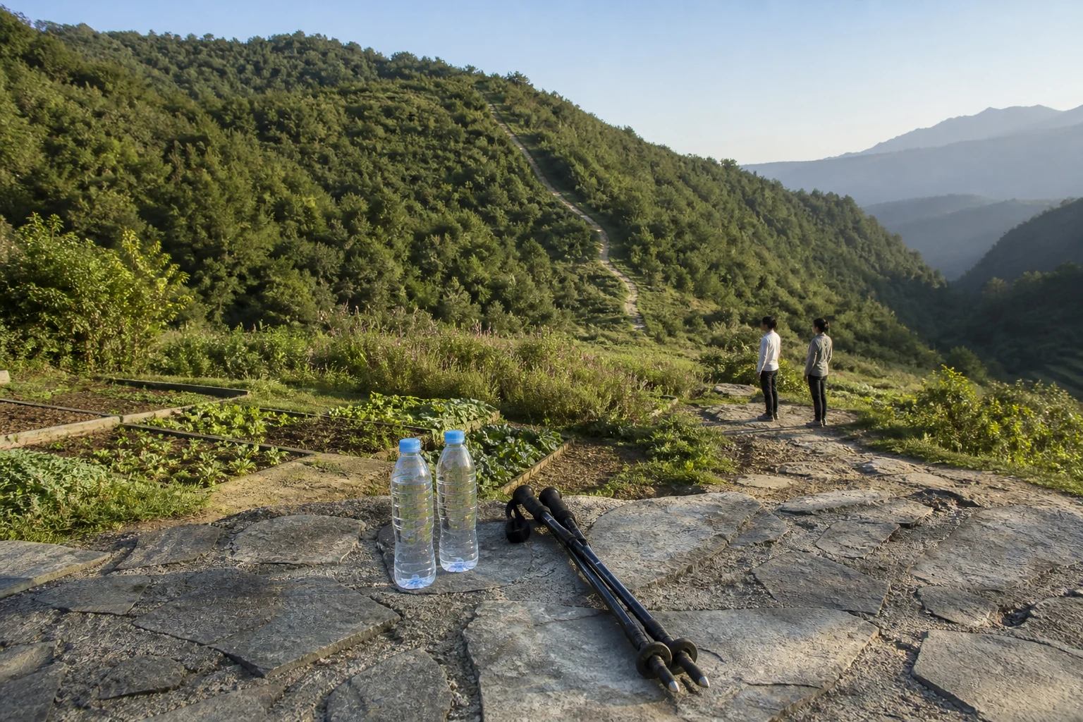Hiking poles and water bottles on a stone wall overlooking a forest valley