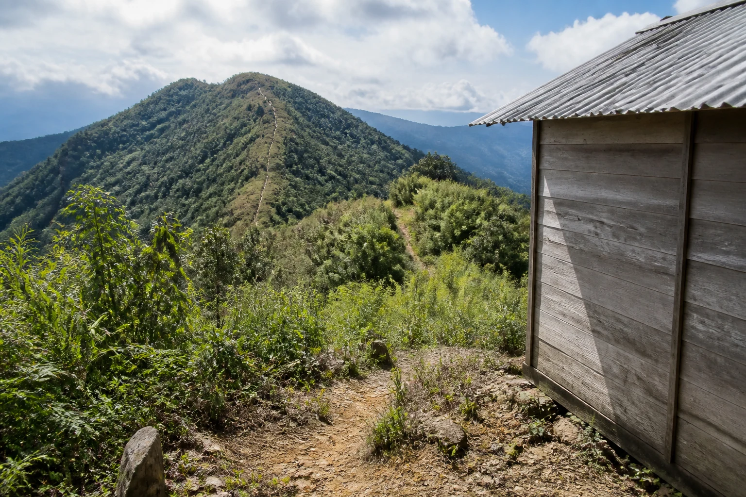Wooden mountain shelter beside a ridge trail in cloud