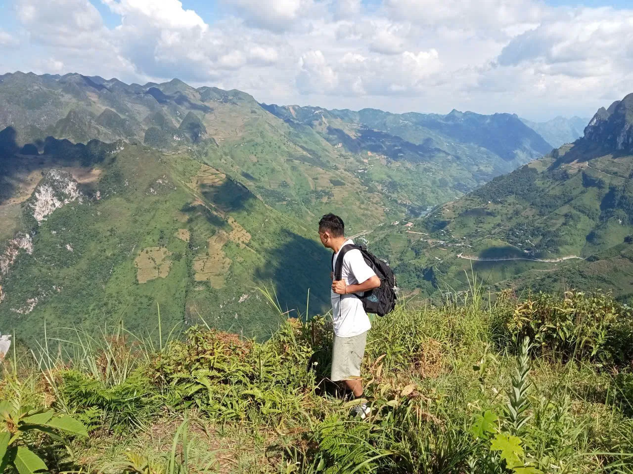 A walker with a daypack on a grassy ridge above a deep canyon and terraced slopes in the Ma Pi Leng area.