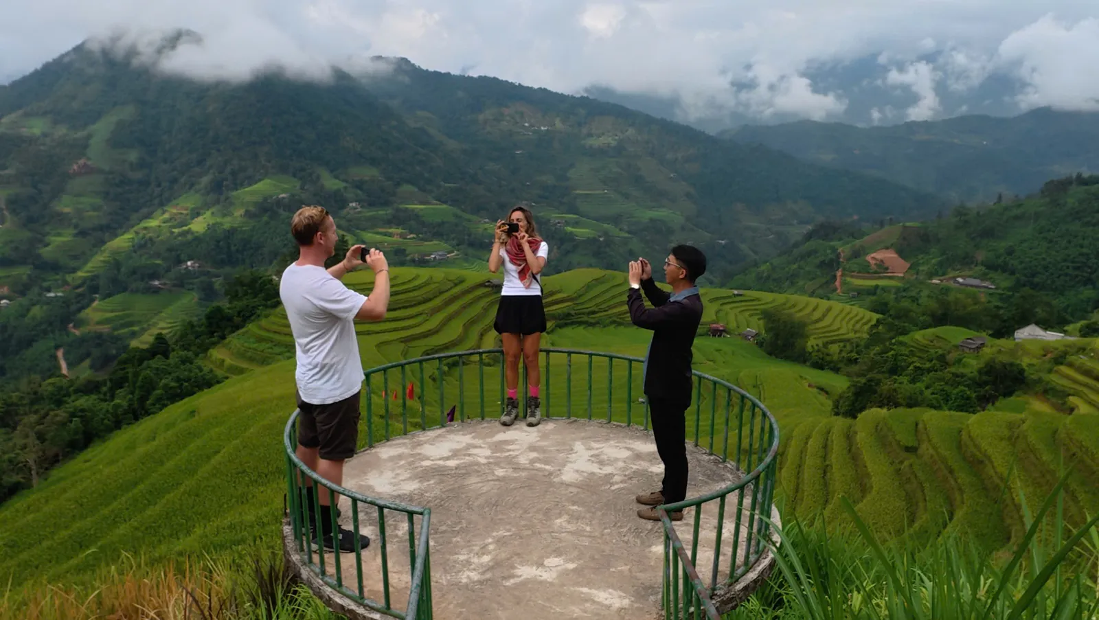 Trekkers and a guide photograph terraced hills from a circular viewpoint near Nam Hong, Hoang Su Phi.