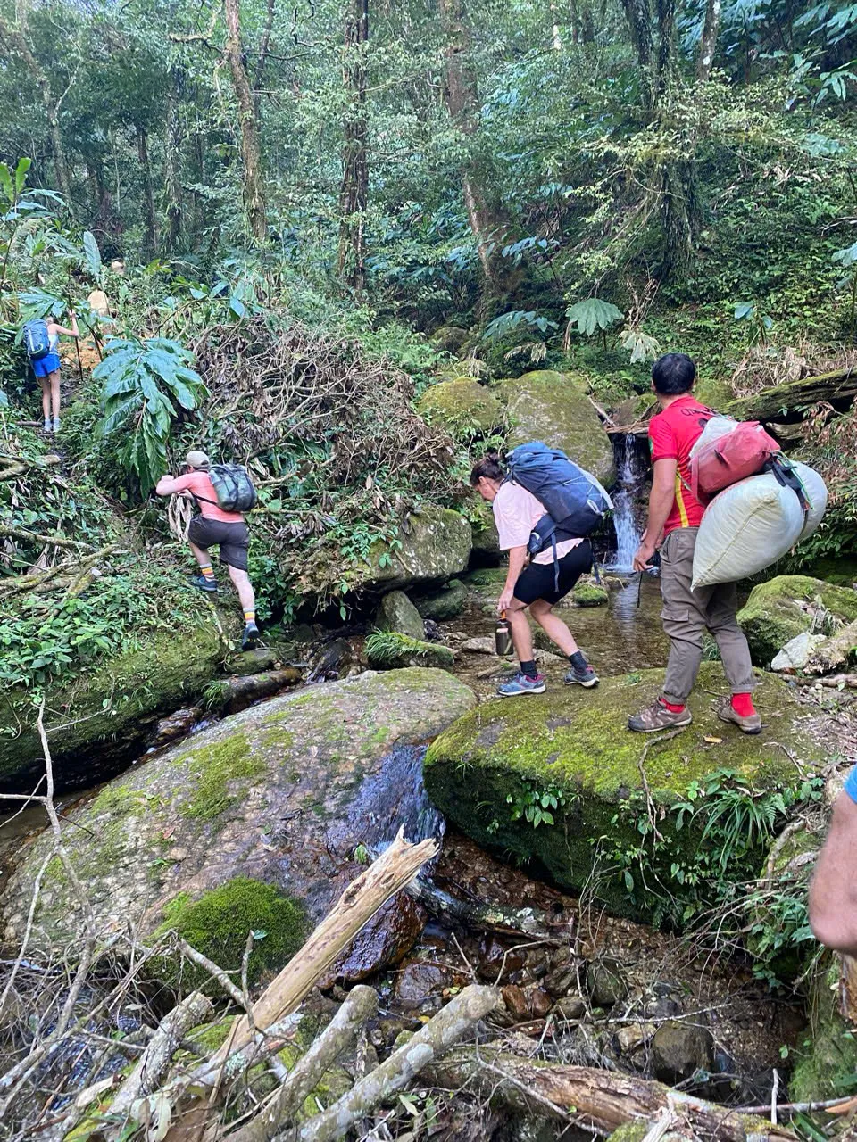 Support team crossing a boulder stream with loads