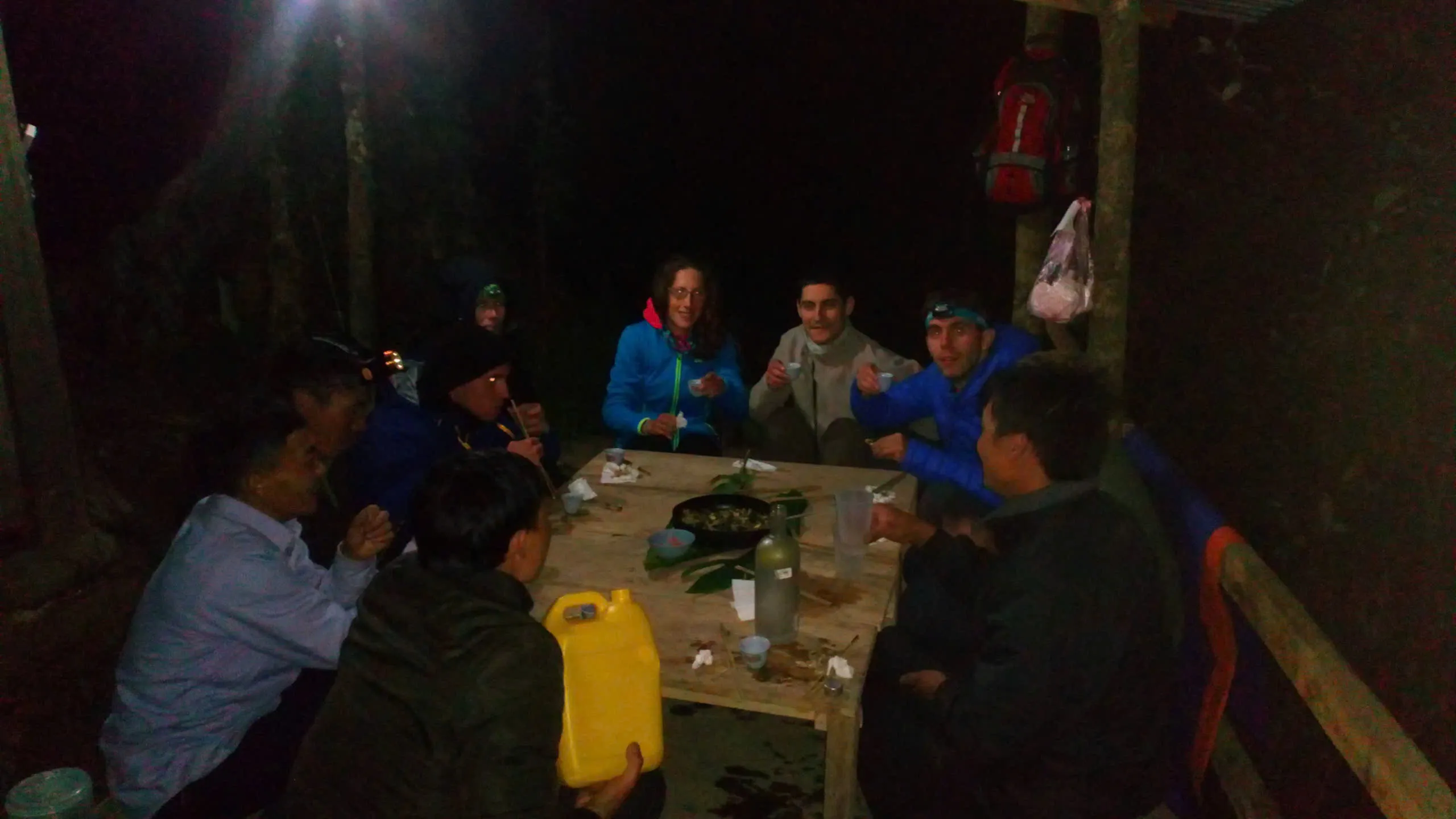 Guests and the local team share dinner around a simple wooden table at the forest shelter.
